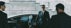 bodyguard in sunglasses opening car door to businessman